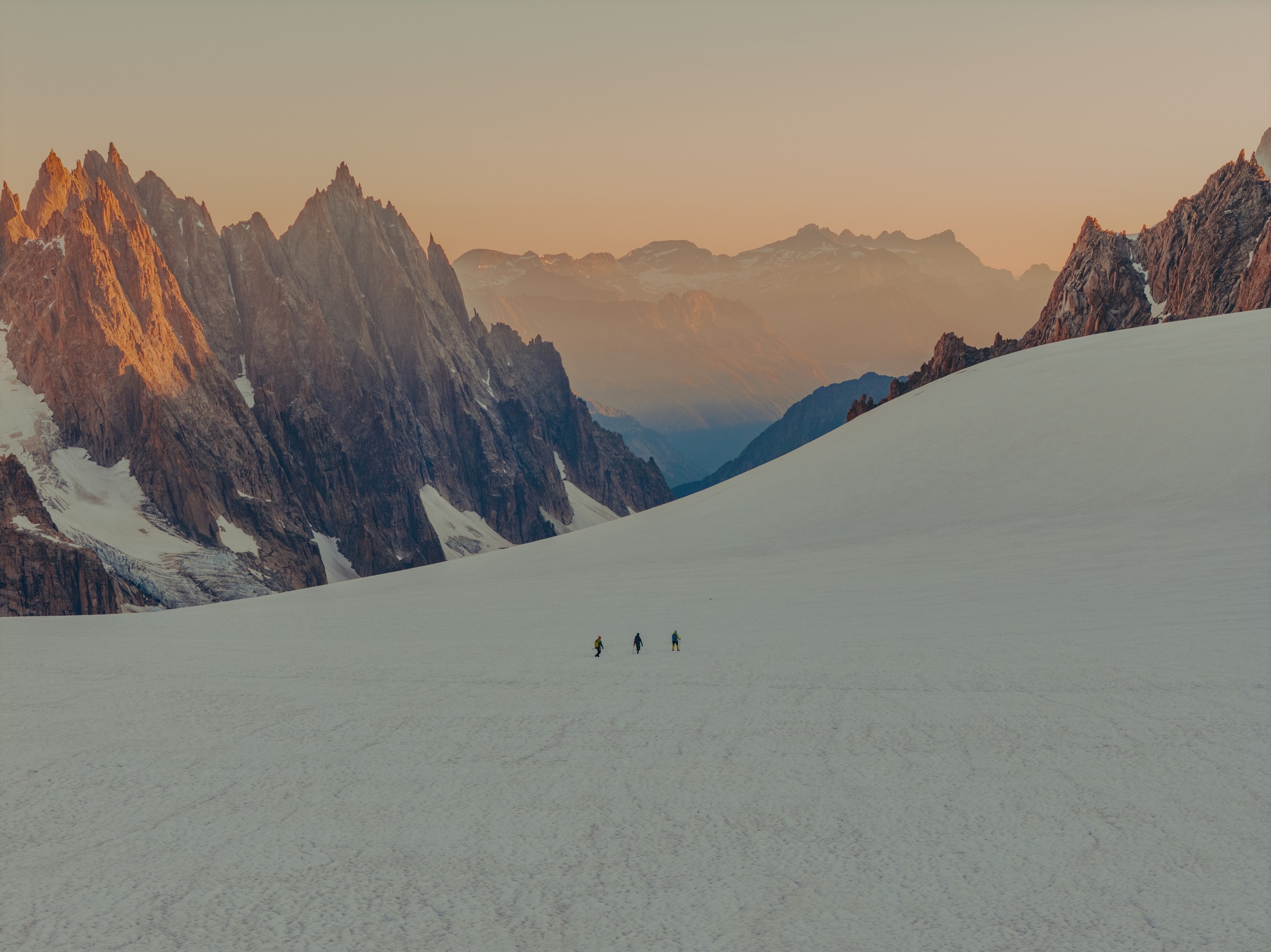 Three people on a glacier surrounded by peaks in golden light