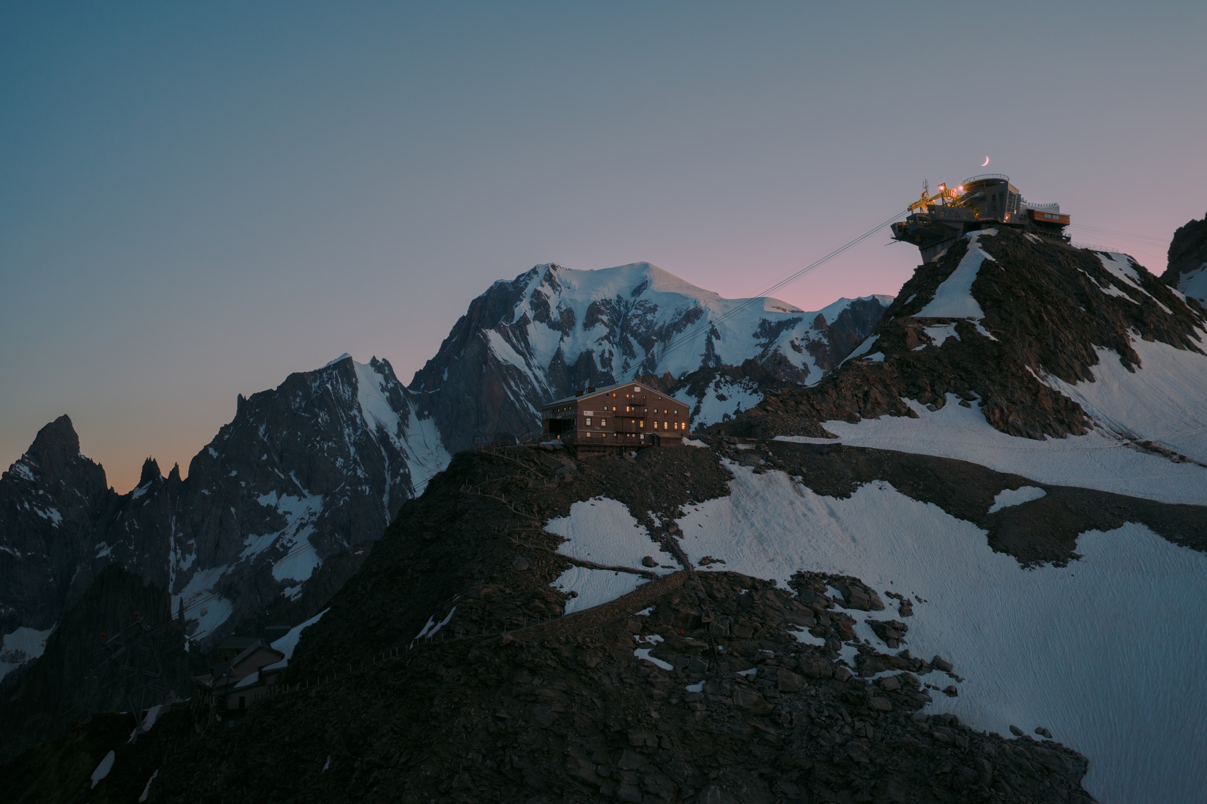 The illuminated hut and Pointe Helbronner station beneath a crescent moon