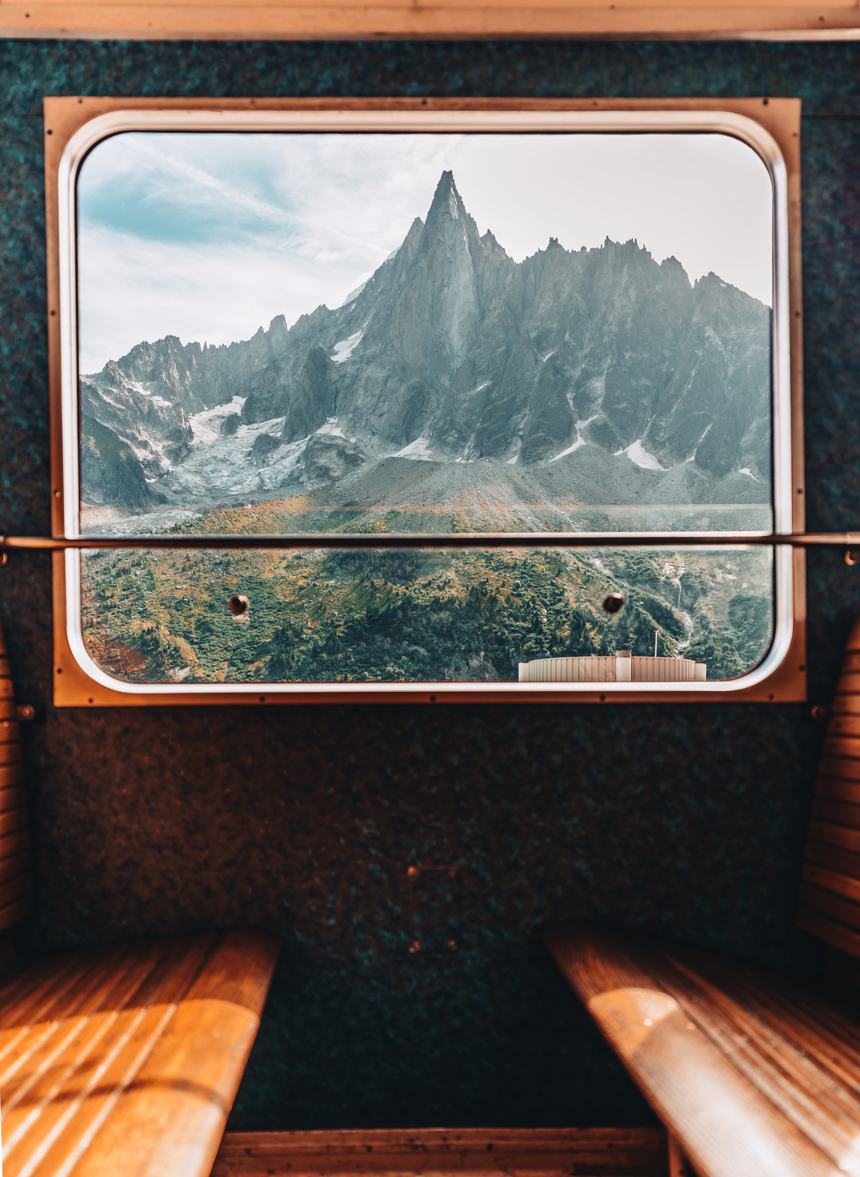 Mountains framed by a train window between two wooden benches