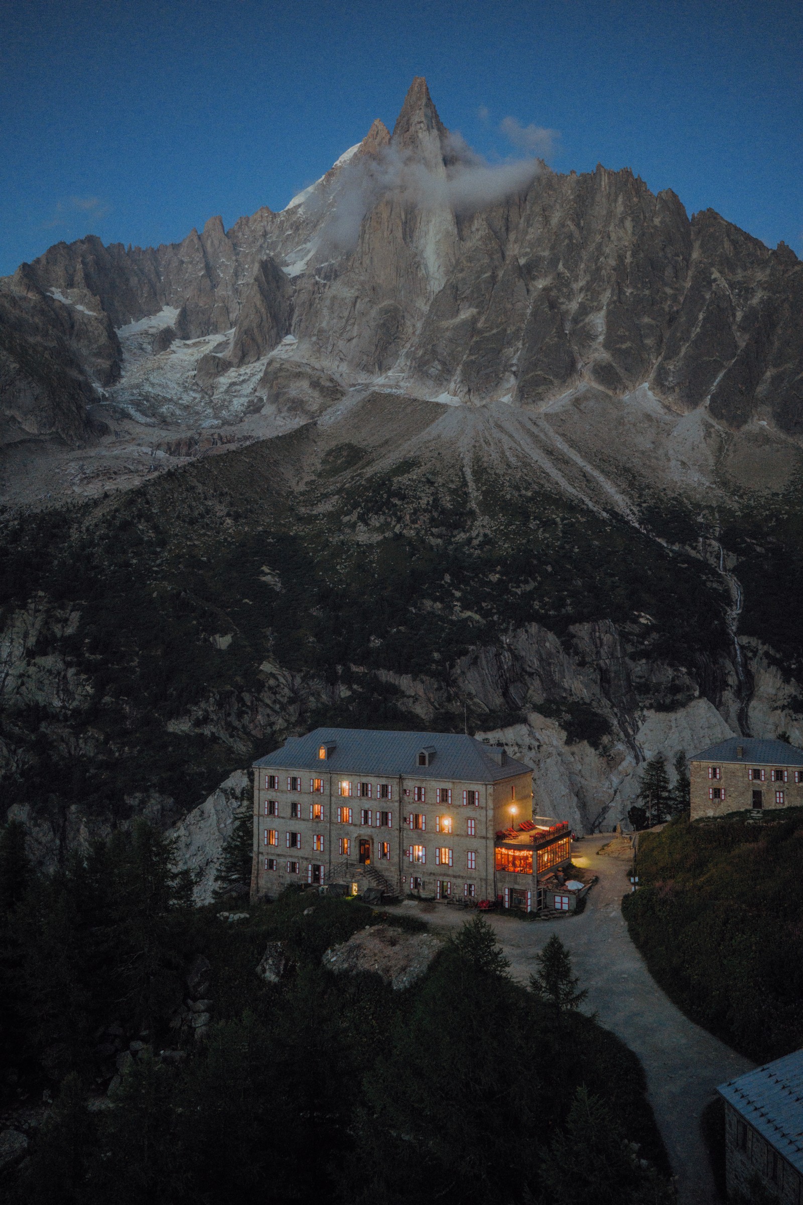 The illuminated windows of the Refuge du Montenvers beneath the mountains at dusk