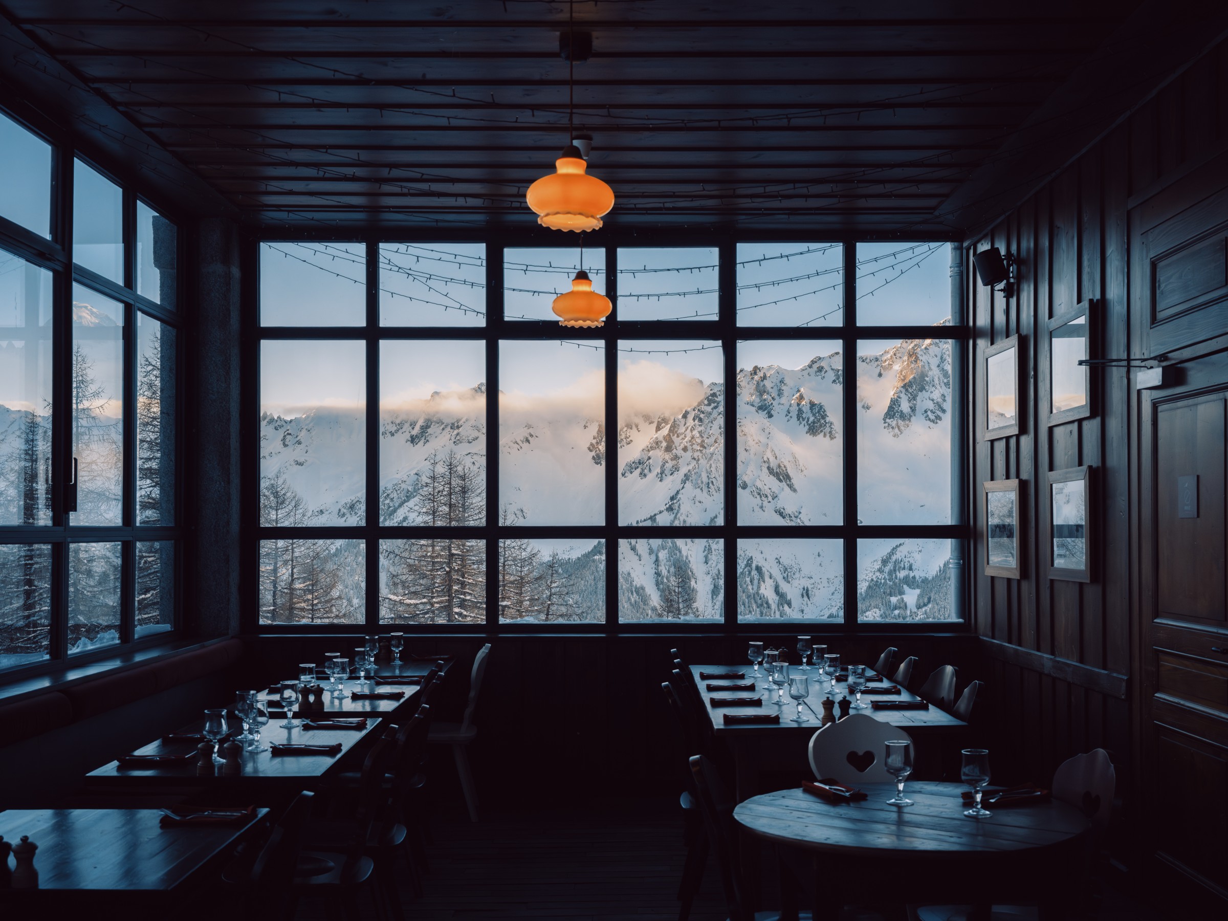 Restaurant tables, amber lamps and a snowy mountain beyond the large windows