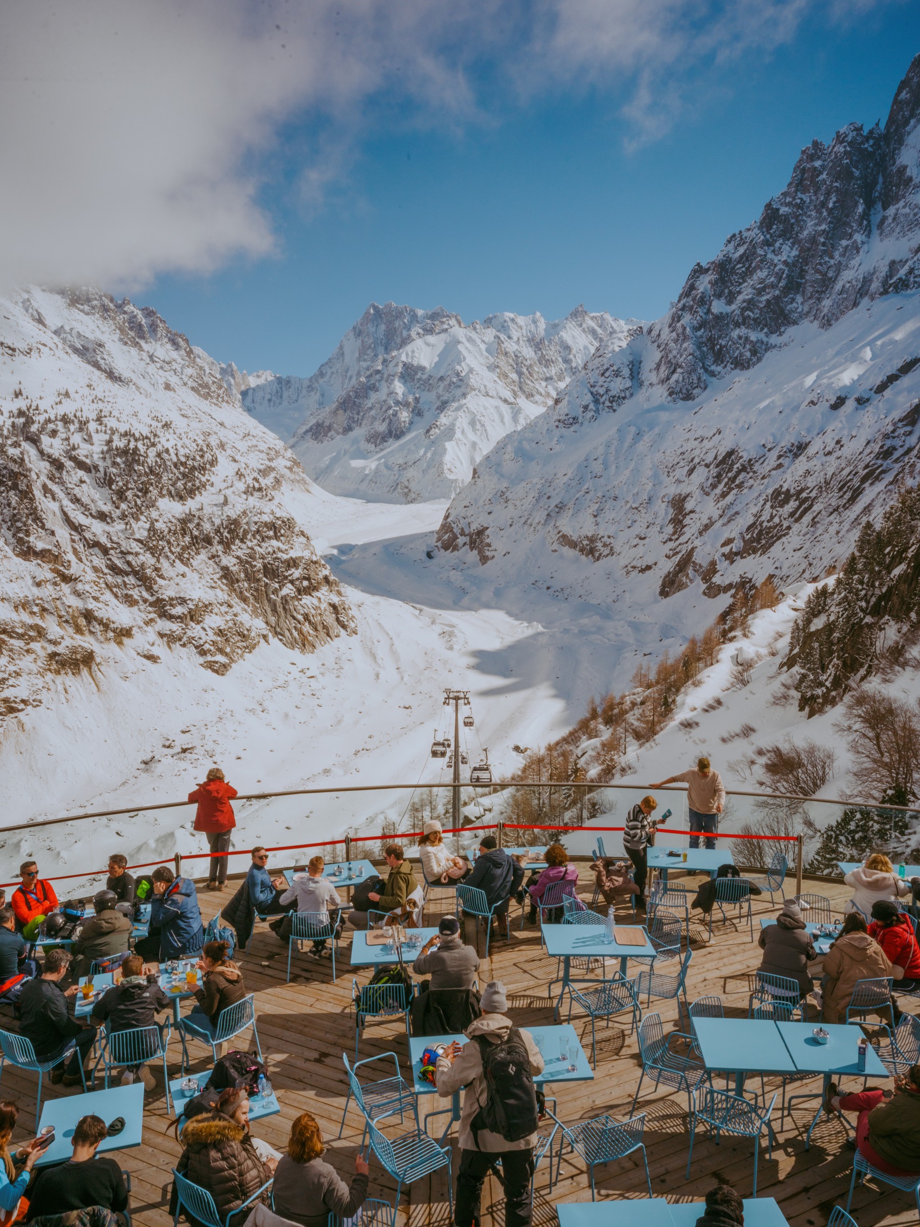 Visitors at blue tables on a terrace overlooking the snowy glacier