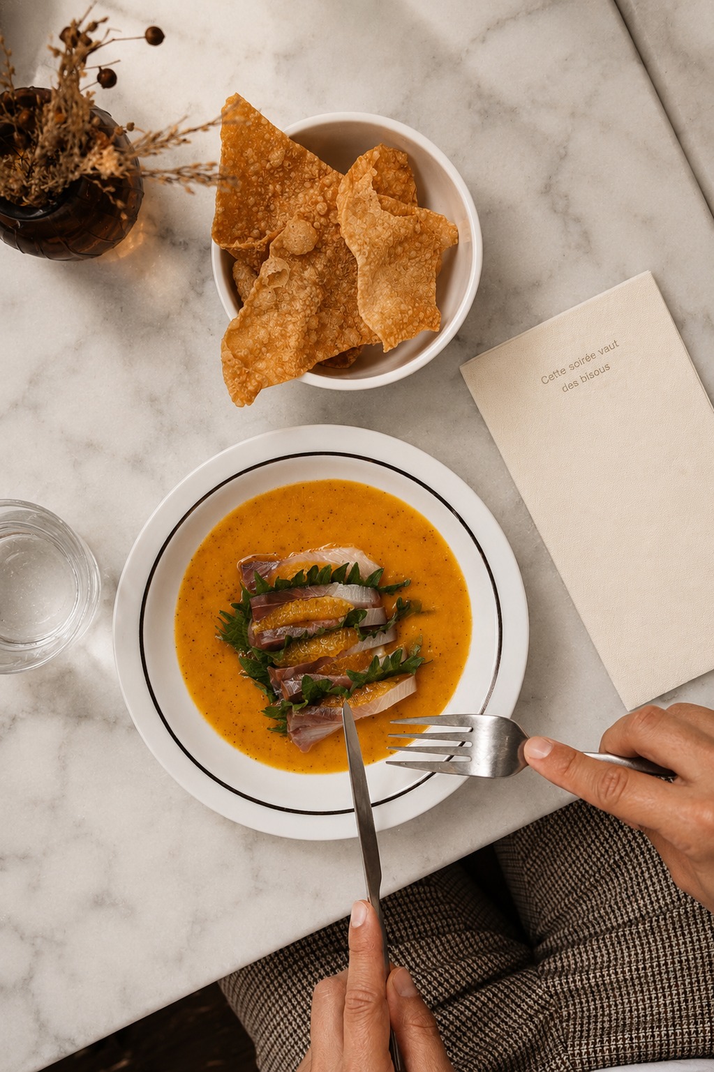 A plated dish with citrus, cutlery and a bowl of crisp wafers