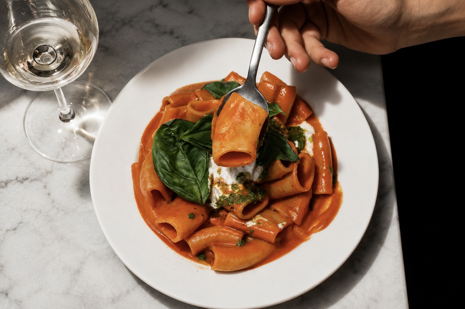 A fork lifting a piece of pasta coated in red sauce above a plate