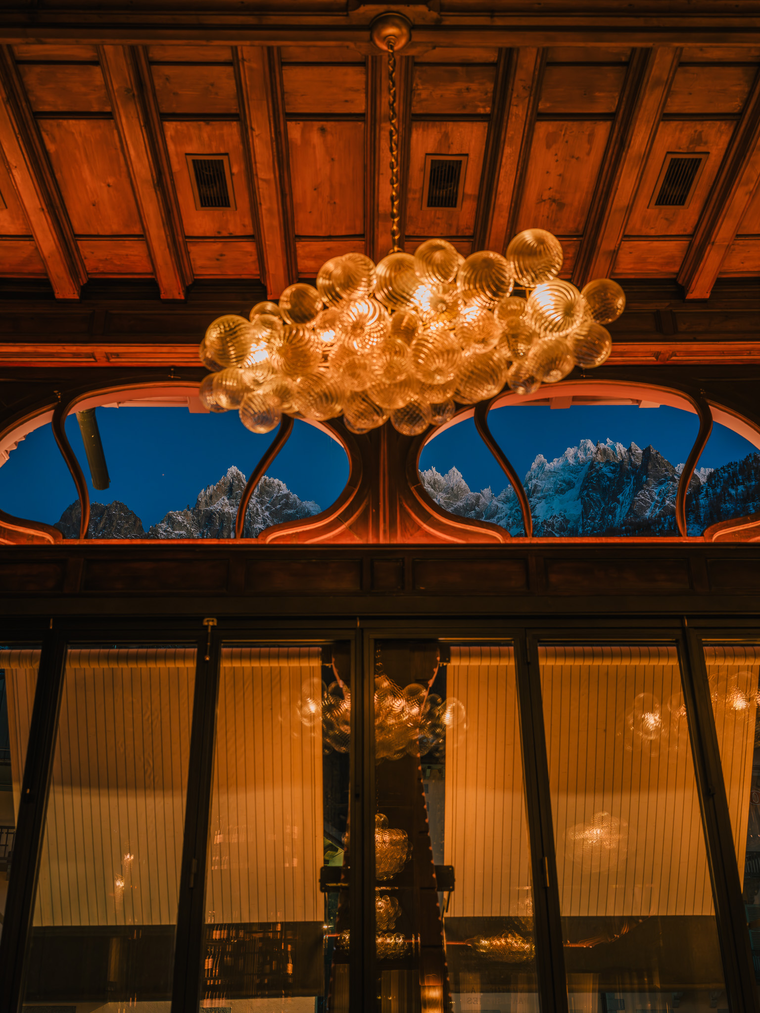 The chandelier and wood panelling at La Rose du Pont, with snowy mountains beyond the windows